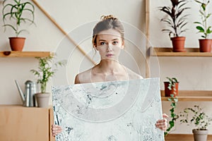 beautiful young naked artist holding picture and looking