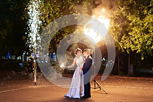 Beautiful young newlywed couple with fire torches in their hands and fireworks 1
