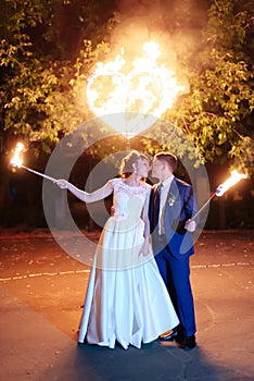 Beautiful young newlywed couple with fire torches in their hands and fireworks 1