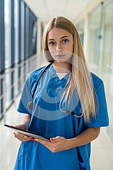 beautiful young nurse with stethoscope and tablet standing in the hallway