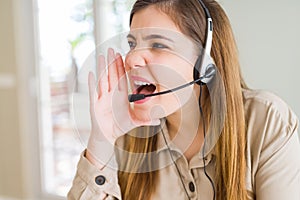 Beautiful young operator woman wearing headset at the office shouting and screaming loud to side with hand on mouth