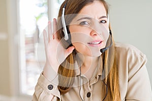 Beautiful young operator woman wearing headset at the office smiling with hand over ear listening an hearing to rumor or gossip