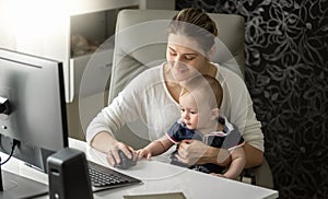 Beautiful young owman working at office and holding her adorable 1 year old baby boy