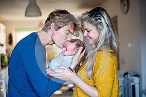 Beautiful young parents with a newborn baby at home, kissing.