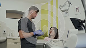 Beautiful young patient is smiling while sitting in chair at the dentist. Handsome dentist showing artificial jaw at the