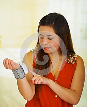 Beautiful young patient using an automatic tensiometer in her arm, in a doctor consulting room background