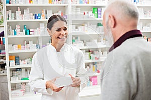 Beautiful young pharmacist selling medications to senior patient