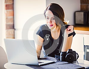 Beautiful young photographer sitting at kitchen with camera