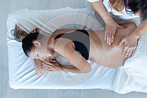 Beautiful young physiotherapist woman massaging tummy on pregnant woman on a stretcher at home