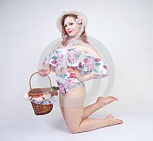 Beautiful young pin up caucasian girl in romantic fashionable straw hat, vintage swimsuit with flowers and retro wicker basket pos