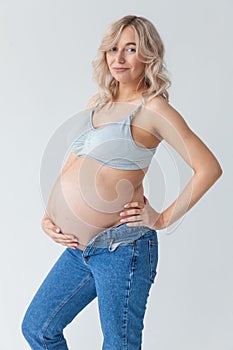 Beautiful young pregnant blonde woman in blue jeans and a top for feeding a baby stands and strokes a big belly
