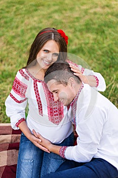 Beautiful young pregnant couple dressed in national ukrainian style having picnic in autumn park. Maternity and family happiness