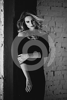 Beautiful young pregnant woman with curls and make-up in a black tight-fitting dress. Black and white photo. Fine art.