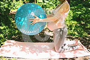 Beautiful young pregnant woman doing yoga exercising with fitness pilates ball in park outdoor. Standing and holding with both