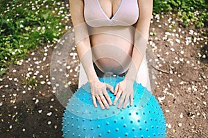 Beautiful young pregnant woman doing yoga exercising with fitness pilates ball in park outdoor. Standing and holding with both