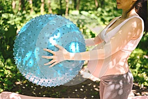 Beautiful young pregnant woman doing yoga exercising with fitness pilates ball in park outdoor. Standing and holding with both