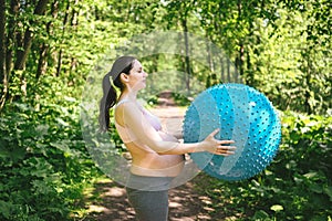 Beautiful young pregnant woman doing yoga exercising with fitness pilates ball in park outdoor. Standing and holding with both