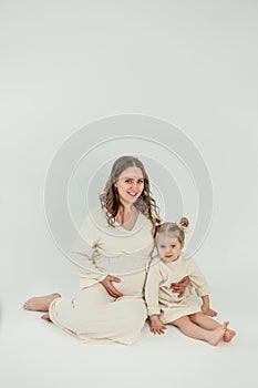 Beautiful young pregnant woman with her little 3 yearold daughter on white background. Stylish pregnant woman in beige dress. photo
