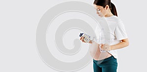Beautiful young pregnant woman holds vitamins pills tablets in her hand and waterbottle . Pregnant Health Concept