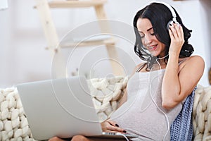Beautiful young pregnant woman with laptop sitting on sofa at home