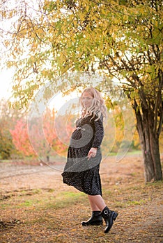 Beautiful young pregnant woman with long blond hair in autumn park in sunny weather