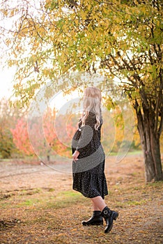 Beautiful young pregnant woman with long blond hair in autumn park in sunny weather