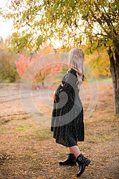 Beautiful young pregnant woman with long blond hair in autumn park in sunny weather