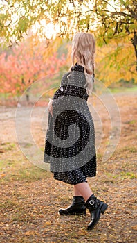 Beautiful young pregnant woman with long blond hair in autumn park in sunny weather