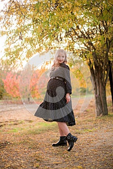 Beautiful young pregnant woman with long blond hair in autumn park in sunny weather