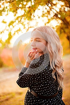 Beautiful young pregnant woman with long blond hair in autumn park in sunny weather