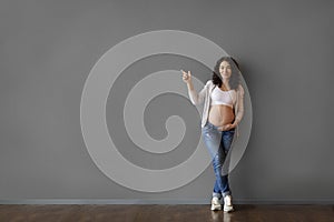 Beautiful Young Pregnant Woman Pointing Aside At Copy Space Over Grey Wall