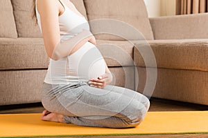 Beautiful young pregnant woman sitting on mat in yoga pose at the home. Pregnancy Yoga and Fitness concept at coronavirus time