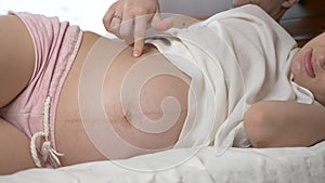 Beautiful, young pregnant woman stroking her belly lying in bed. 4k. Slow motion