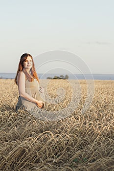 Beautiful young pregnant woman walks on wheat field at sunset, expectant mother with relax in nature stroking her belly with hand