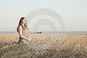 Beautiful young pregnant woman walks on wheat field at sunset, expectant mother with relax in nature stroking her belly with hand