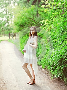 Beautiful young pregnant woman in white dress outdoors