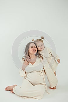 Beautiful young pregnant woman with her little 3 yearold daughter on white background. Stylish pregnant woman in beige dress. photo