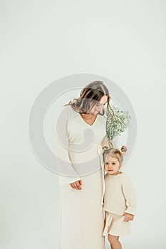 Beautiful young pregnant woman with her little 3 yearold daughter on white background. Stylish pregnant woman in beige dress. photo