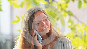 Beautiful young pretty girl in blue shirt with phone in blue case talking outdise on a summer day stable shot