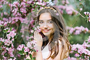 A beautiful young pretty girl with long hair loose stands near the blooming spring Bush of weigela with pink flowers. She touches