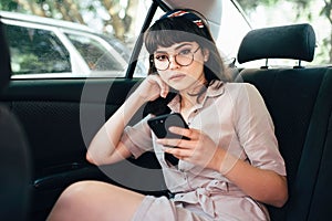 Beautiful young pretty girl is using a smart phone and smiling while sitting on back seat in the car