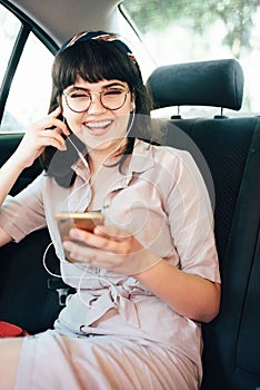 Beautiful young pretty girl is using a smart phone and smiling while sitting on back seat in the car