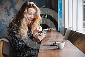 Beautiful young pretty woman sitting in cafe indoors using laptop computer and mobile phone