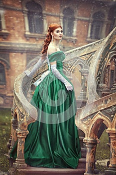 Beautiful, young, red-haired girl in a green medieval dress, climbs the stairs to the castle. Fantastic photosession.