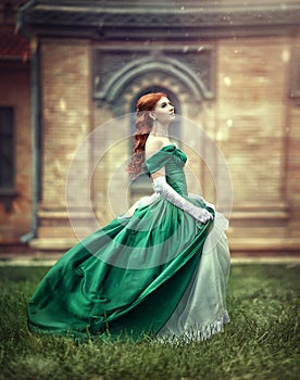 Beautiful, young, red-haired girl in a green medieval dress, climbs the stairs to the castle.
