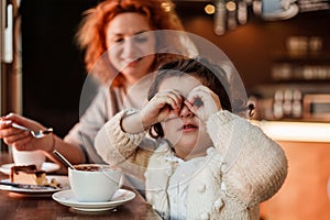 Beautiful young red-haired mother with cute curly-haired daughter are sitting in cozy cafe and drinking hot school. Mothers Day.