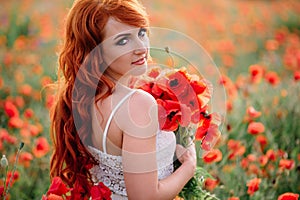 Beautiful young red-haired woman in poppy field holding a bouquet of poppies