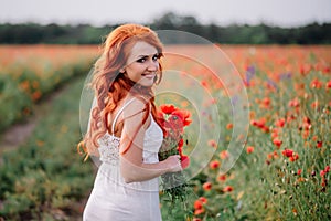 Beautiful young red-haired woman in poppy field holding a bouquet of poppies