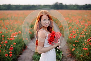 Beautiful young red-haired woman in poppy field holding a bouquet of poppies