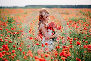 Beautiful young red-haired woman in poppy field holding a bouquet of poppies